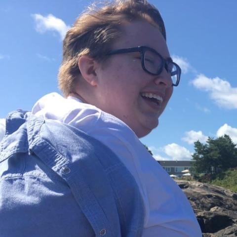 A light-skinned non-binary person wearing black glasses and a white shirt smiles wide.