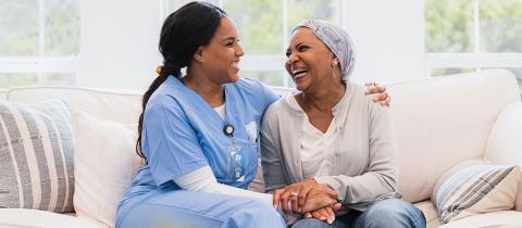 Adult female hospice nurse smiles as she embraces her female senior adult cancer patient