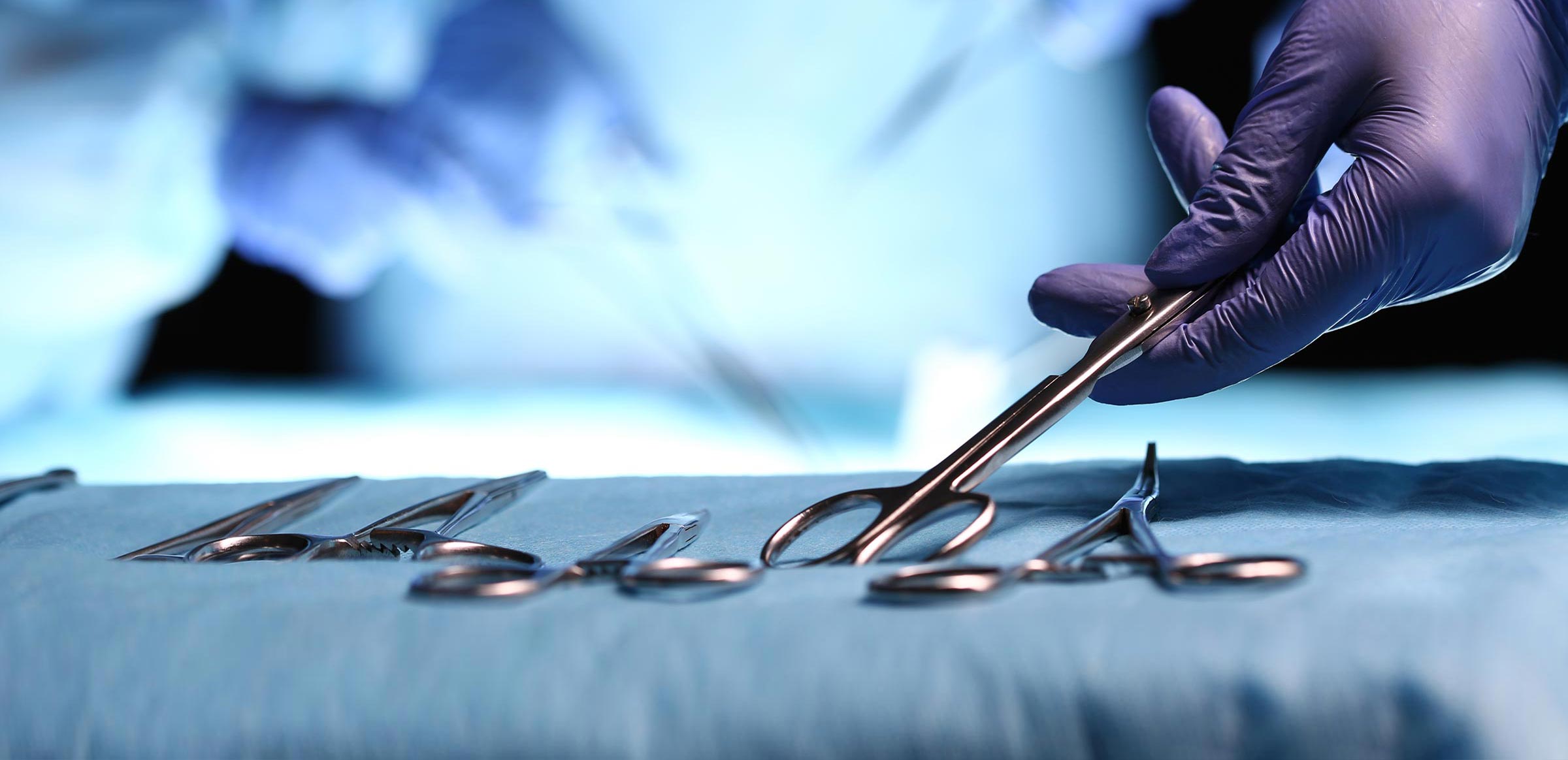 A gloved hand taking a surgical tool off of a tray of tools