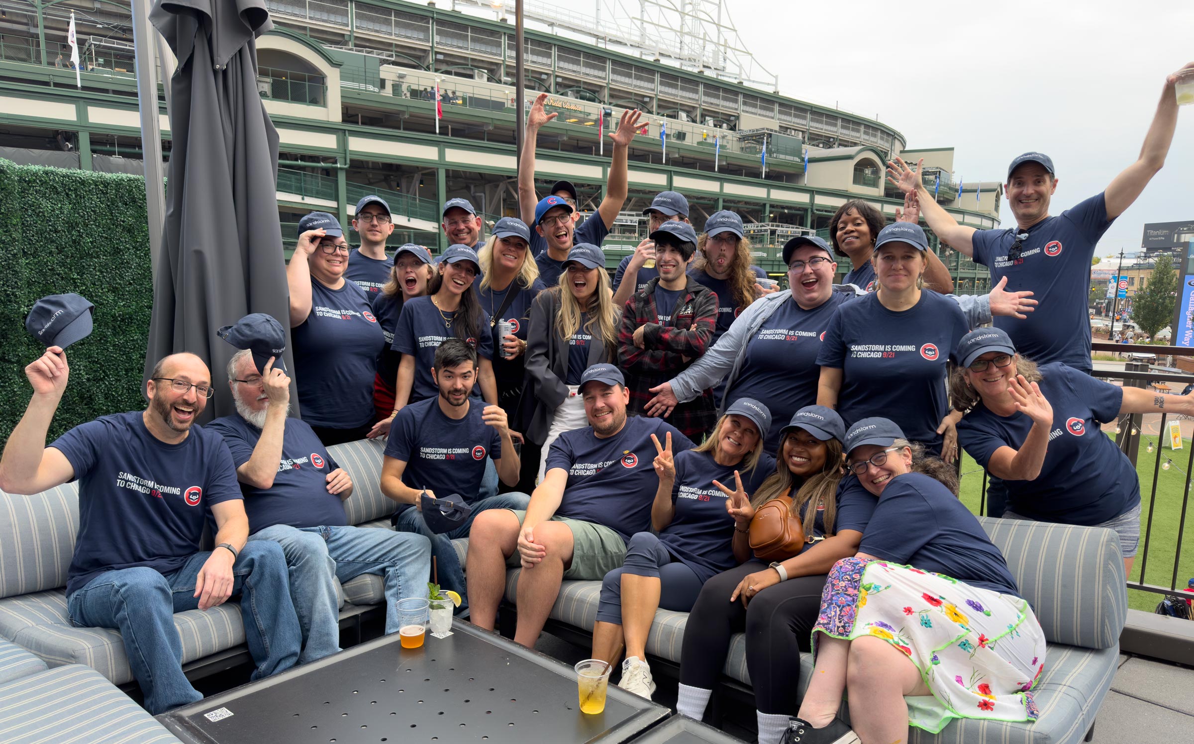 A large crowd of Sandstorm staff in matching shirts and hats with Wrigley Field in the background