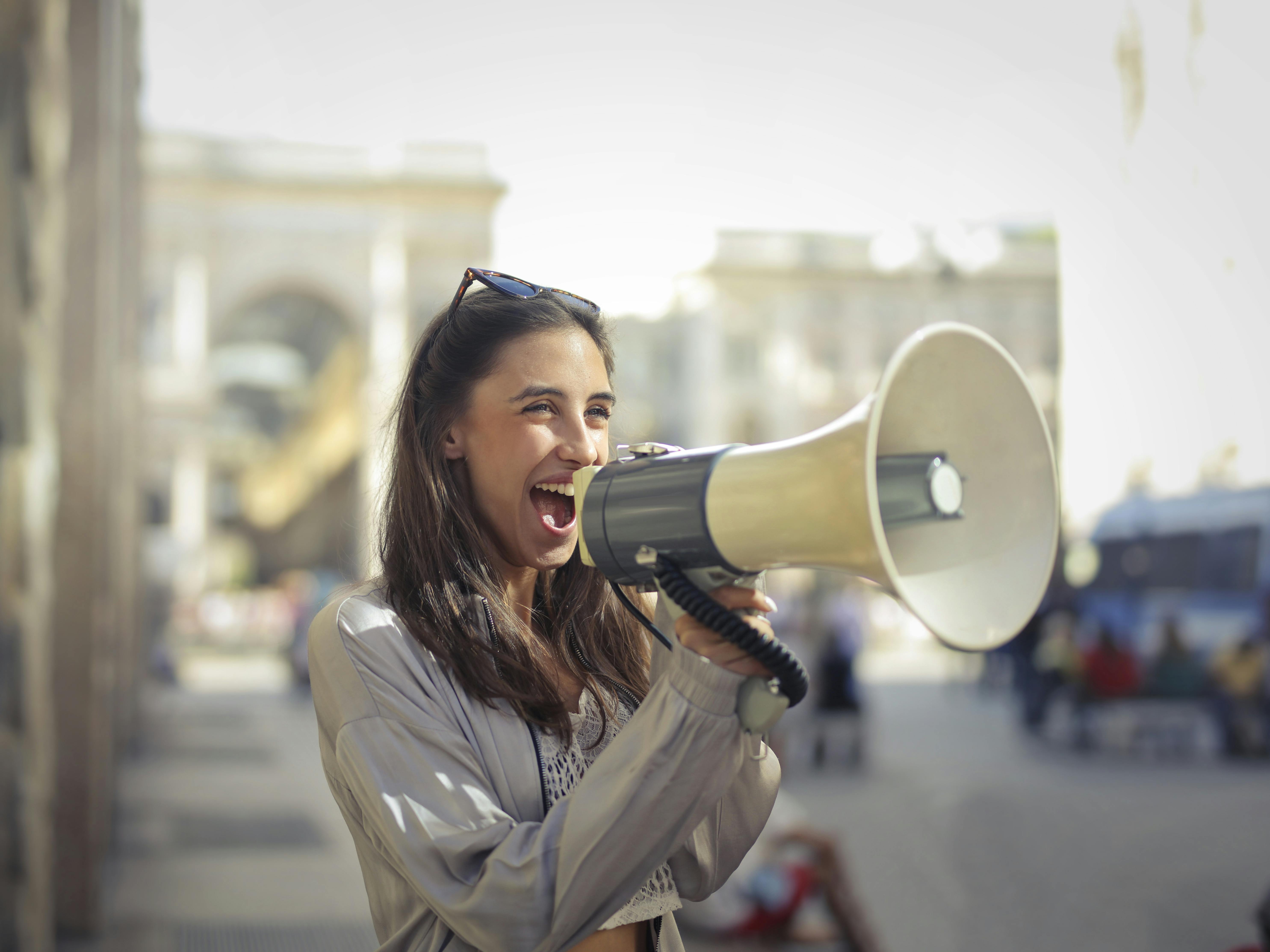 Light skinned female presenting brunette using a megaphone on a crowded streat