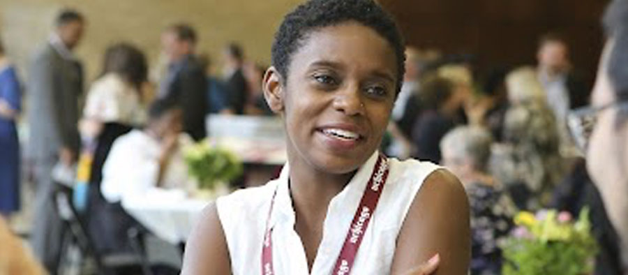 A dark-skinned feminine-presenting person wearing a UChicago lanyard smiles and speaks to someone out of frame at a Crown Family School event.