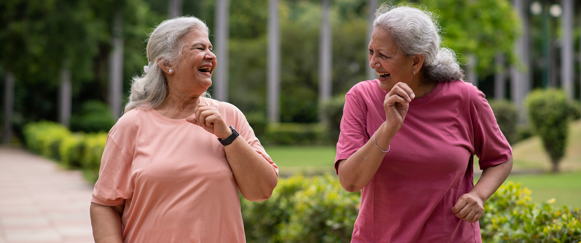 Two older women laughing and walking outdoors in a park.