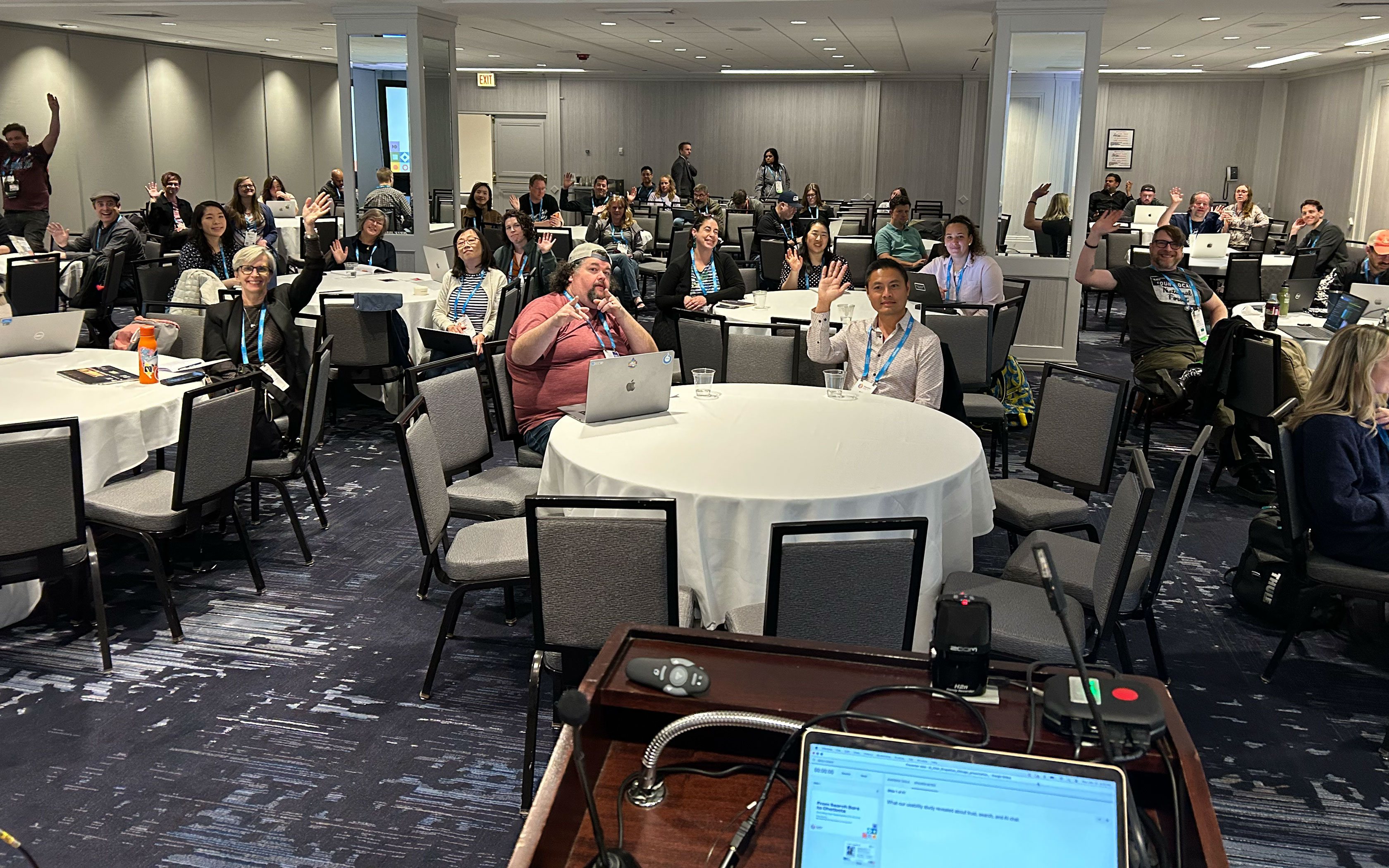 Conference room with DrupalCon attendees seated at round tables.