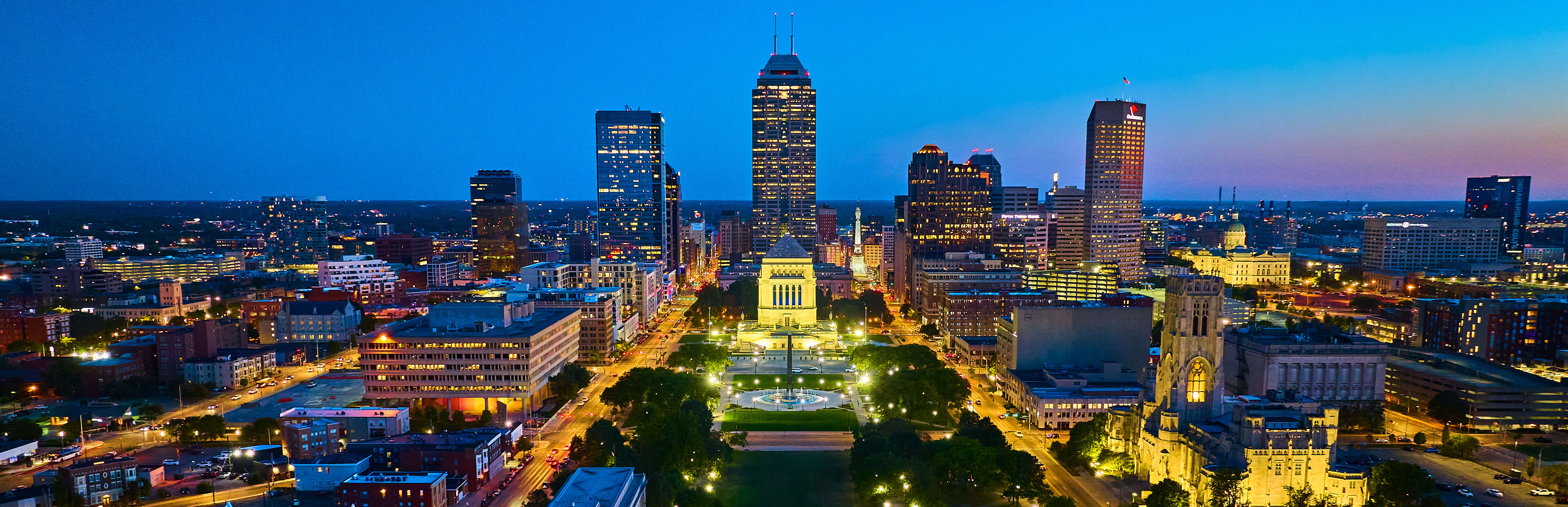 Skyline of a Indianapolis at dusk with illuminated buildings and a clear blue sky.