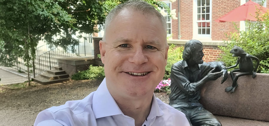 Chad Capellman taking a selfie outdoors on the University of Maryland campus, with the Jim Henson and Kermit the Frog bench statue behind him.