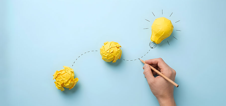 Crumpled paper leads to a bright lightbulb drawn by a hand on blue background.