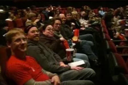 A group of people sitting in a movie theater smile towards the camera.