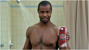 A male-presenting person holding Old Spice in a shower.