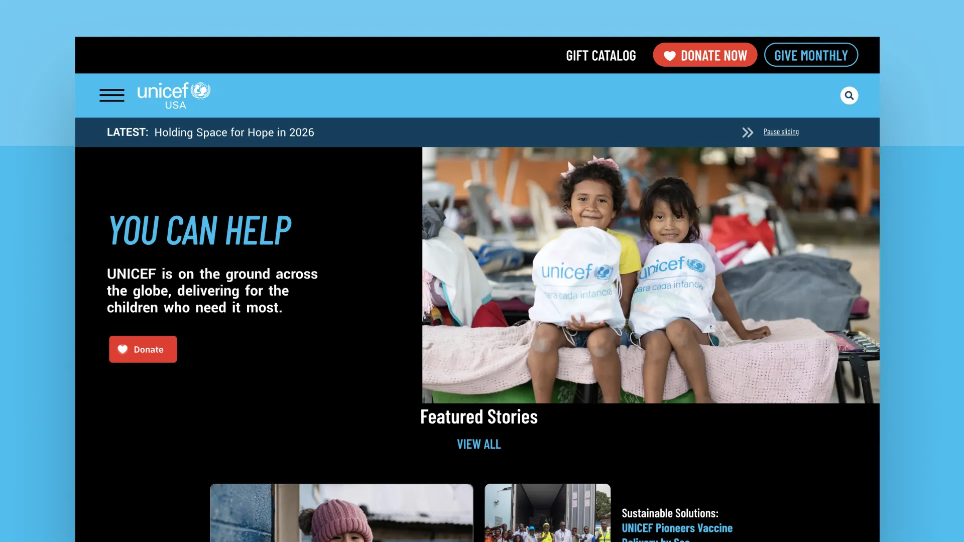 Two children smiling, wearing UNICEF t-shirts, sitting on a cot.
