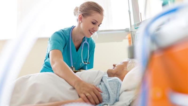 Female nurse smiling and assisting an elderly patient.
