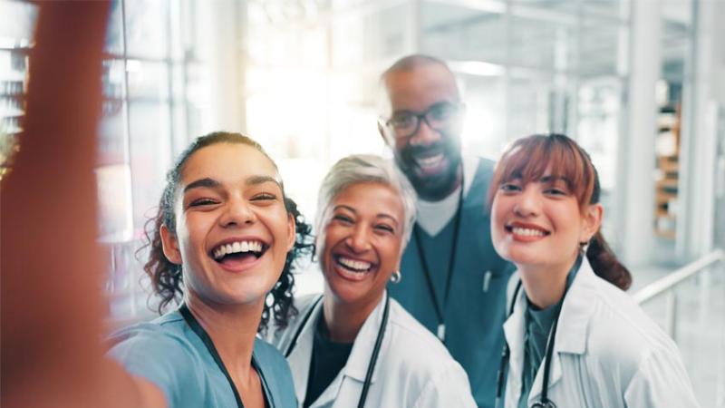 Four medical professionals stand together, smiling as they take a selfie.