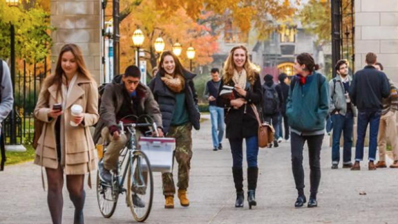 Students walking on campus during autumn, colorful leaves in the background.