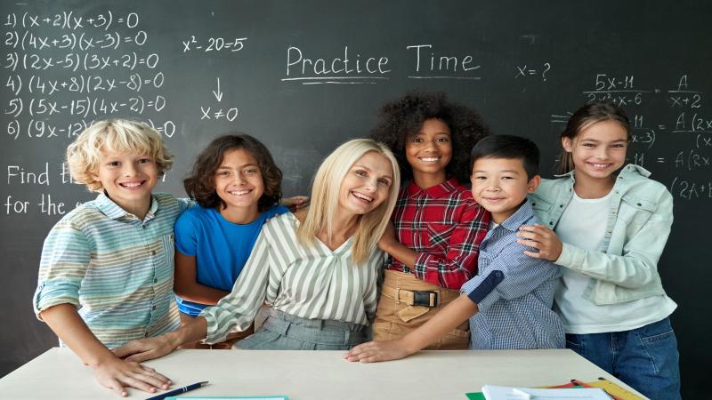 Teacher and five smiling children pose in front of a chalkboard with math equations.