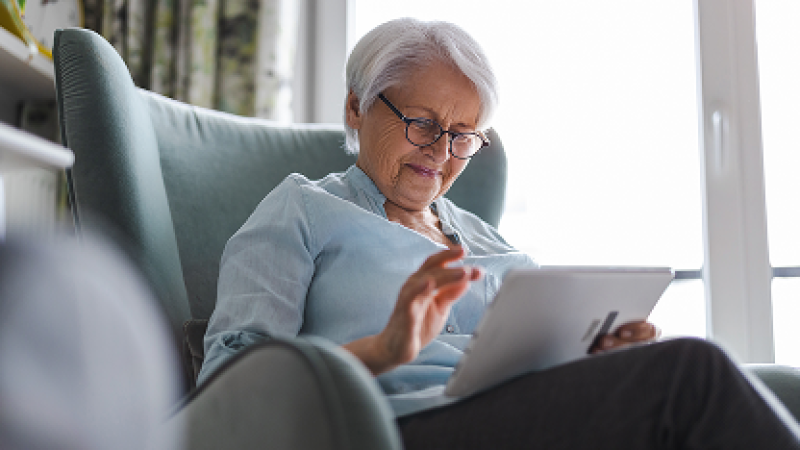 Older woman using a tablet in an armchair, looking focused.