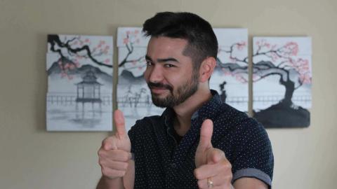 Josh Hunter is a light skinned male with black hair, mustache, and beard wearing a blue and white polka dot shirt pointing with both fingers at the viewer with a picture of a cherry blossom tree in the background