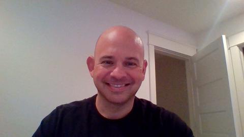 Mike Marsico a light skinned male with a bald head wearing a black t-shirt smiling at the camera