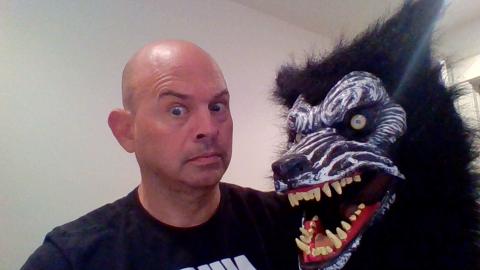 Mike Marsico a light skinned male with a bald head wearing a black t-shirt with a concerned look as a scary wolf head appears from the right
