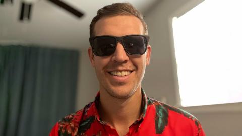 Nathan Haas is a light skinned male with brown hair, sun glasses, light stubble wearing a red Hawaiian print shirt with a window in the background