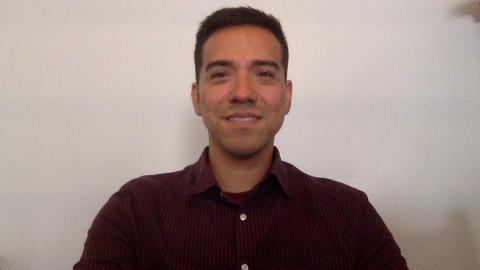 Nico Tellez is a medium skinned male with dark brown hair wearing a red button down shirt smiling at the camera