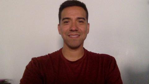 Nico Tellez is a medium skinned male with dark brown hair wearing a red t-shirt shirt smiling at the camera