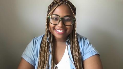 Sandie Starr is a dark skinned female with blond and brown braids with glasses wearing a white shirt with a jean short sleeve jacket over top