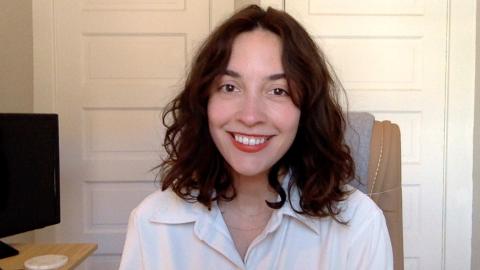 Hannah Sheridan a light skinned female with shoulder length curly brown hair wearing a white shirt holding smiling at the camera