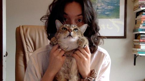 Hannah Sheridan a light skinned female with shoulder length curly brown hair wearing a white t-shirt holding her grey stripped cat Norman
