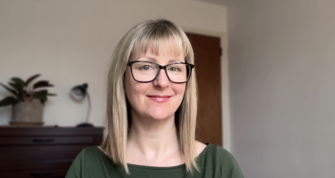 Amber Reeves is a light skinned female with shoulder length blonde hair, black glasses, wearing a green shirt smiling at the camera