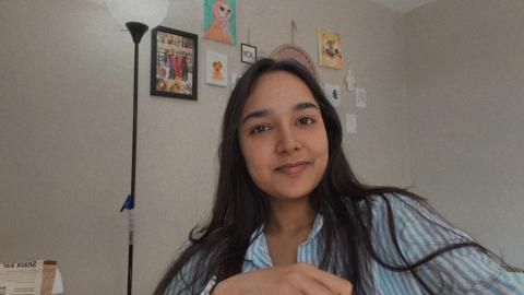 Isha is smiling in a room with art on the walls and a floor lamp