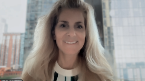 Kathryn is smiling at the camera and has long blond hair with city buildings behind her.