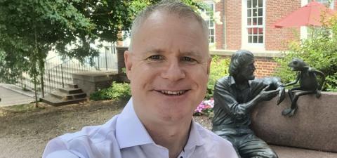 Chad Capellman taking a selfie outdoors on the University of Maryland campus, with the Jim Henson and Kermit the Frog bench statue behind him.