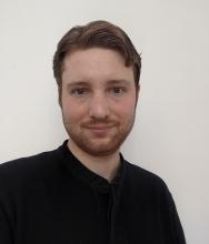 David Boocock a light skinned male with red hair and red facial hair wearing a black shirt on a white background