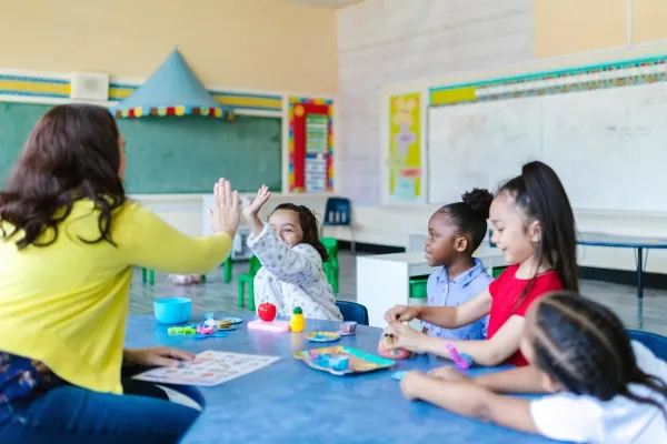 A teacher high fives a student while sitting at a table with 3 other students