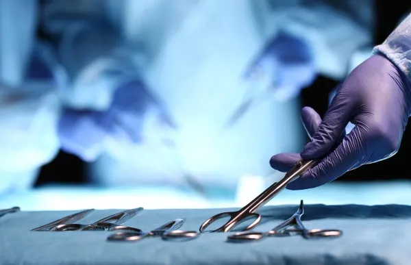 A gloved hand taking a tool from a tray of surgical equipment