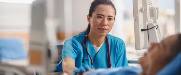 Nurse with olive-toned skin and blue scrubs sitting beside patient