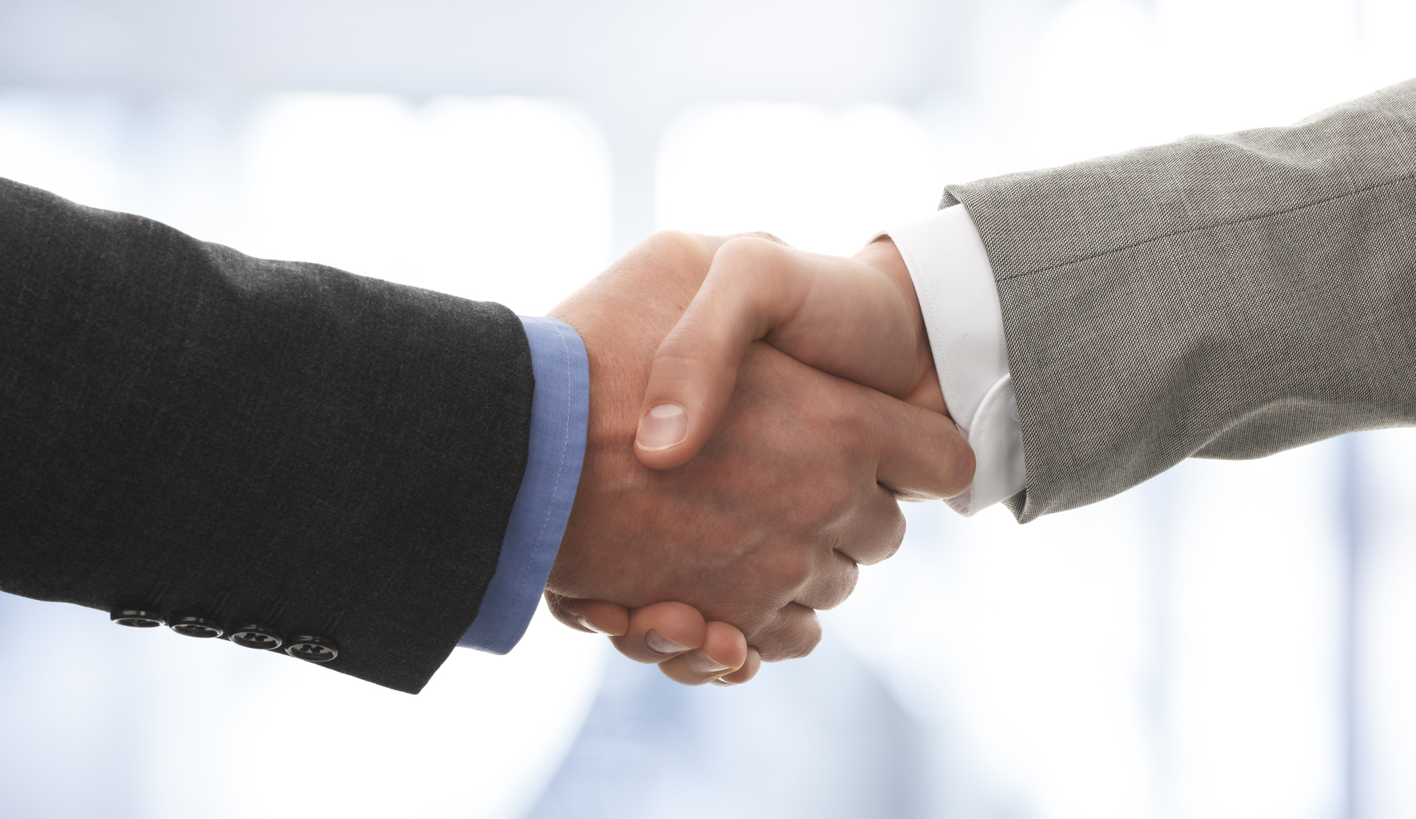A closeup of two people in business suits shaking hands.