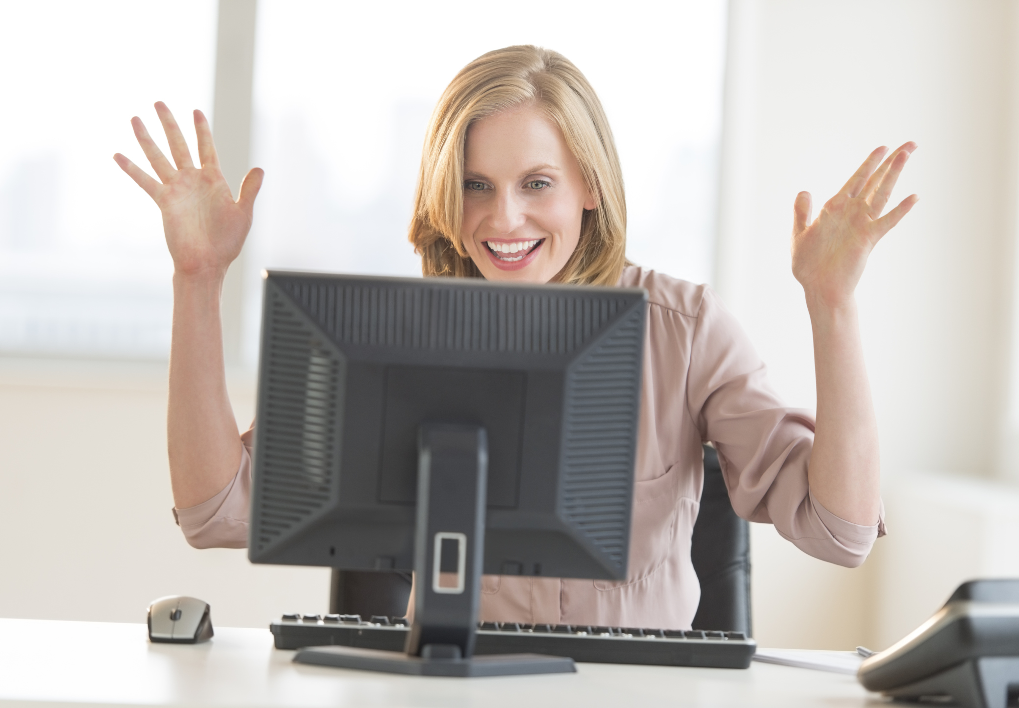 female presenting individual sitting in front of a computer screen looking surprised with their hands up